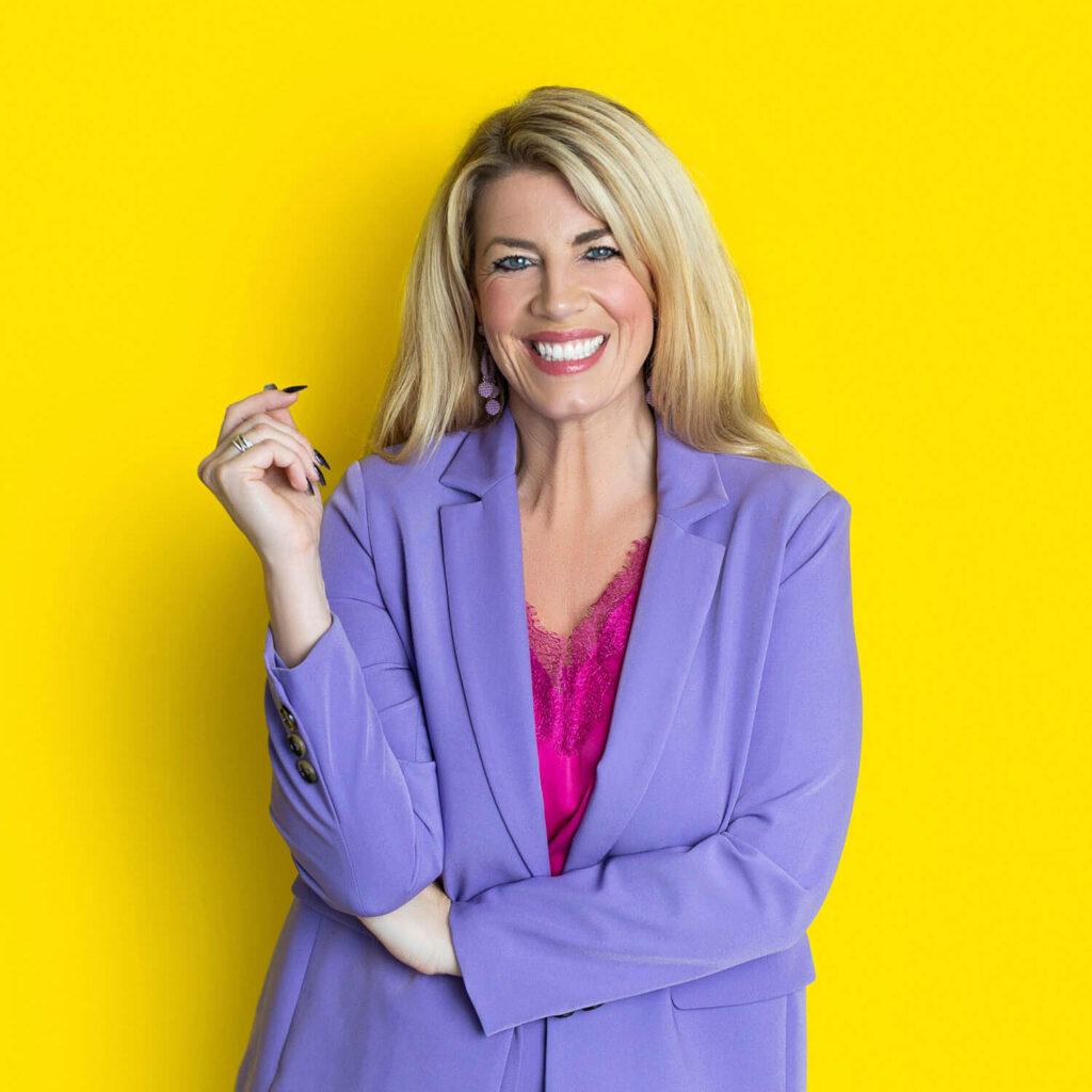 A woman in a lilac suit poses confidently against a bold yellow background, photographed for a bright and modern brand portrait.