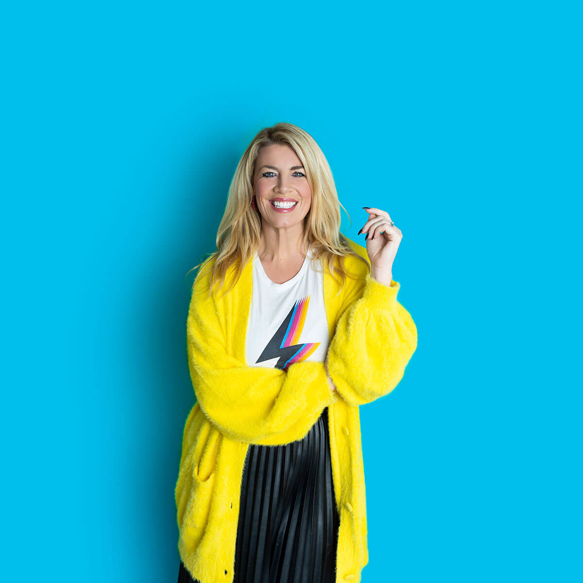 Approachable and friendly looking business coach in yellow fluffy cardigan, smiling against a turquoise blue background, colourful brand photography