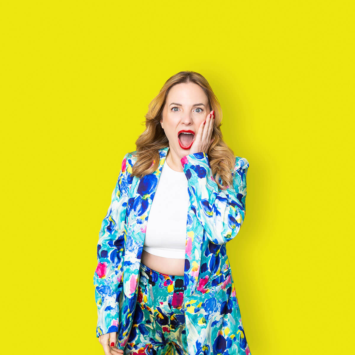 Studio personal branding portrait of a woman in a colourful suit against a yellow background, using expressive body language to represent confidence and personality
