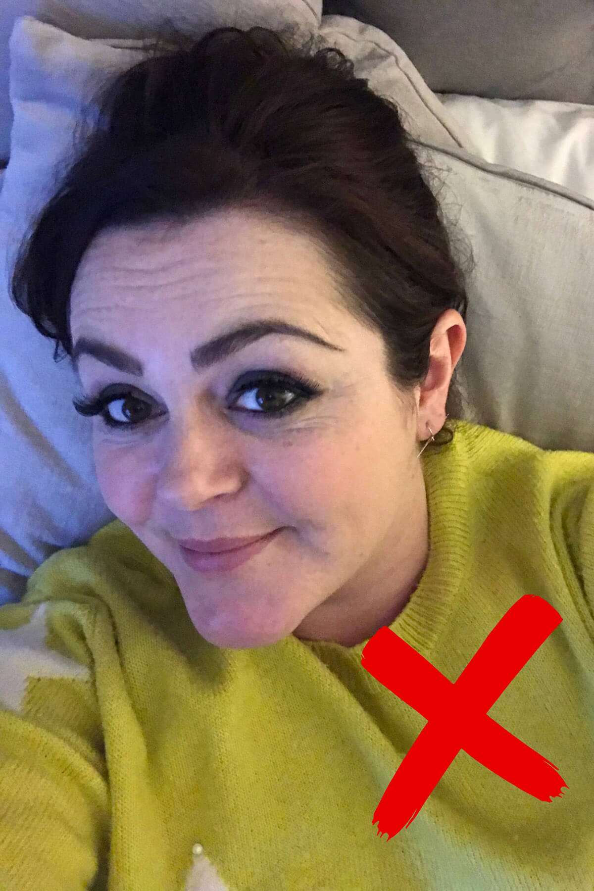 Example of unflattering high phone angle selfie marked with red X, showing camera held too far above face while lying on sofa creating awkward foreshortening – demonstrating common selfie angle mistake to avoid