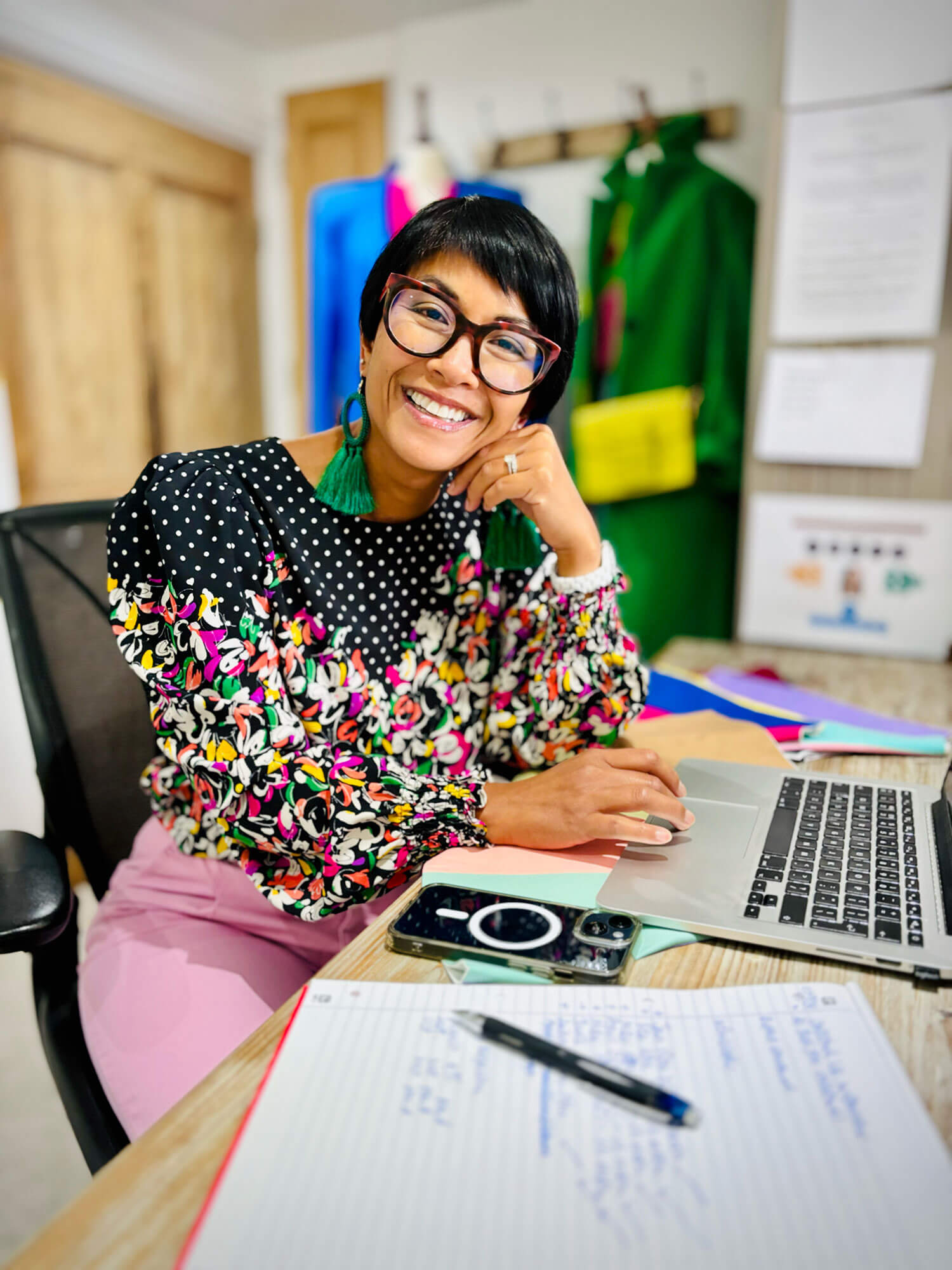 Personal stylist Chantelle Znideric who has with short dark hair and glasses sits at her desk working on her blog with notebook and phone. 