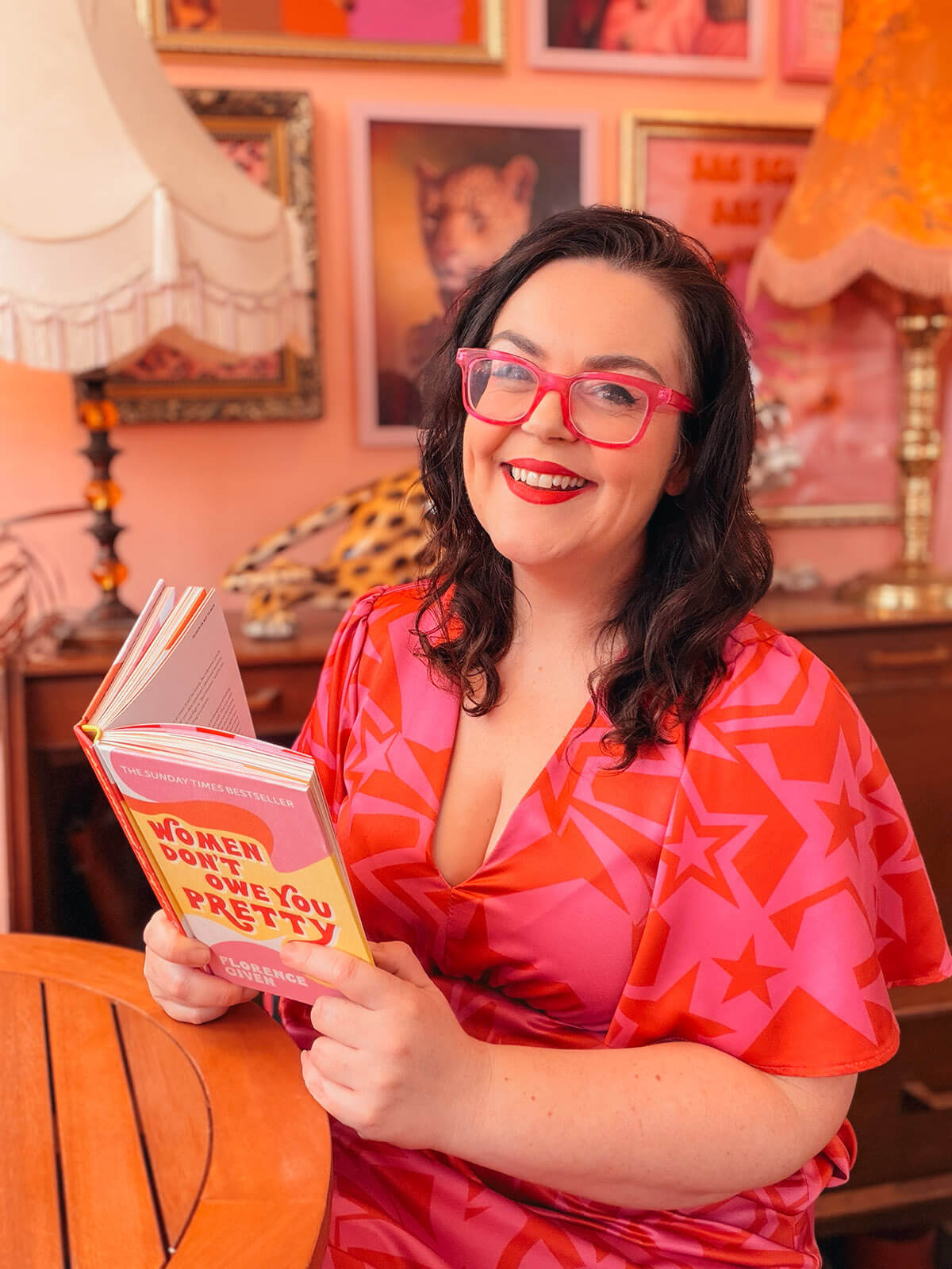 Brand photographer Rosie Parsons wearing pink glasses and a star-print dress, reading a book in a vibrant pink styled room - inspiration for how to start a blog for beginners.