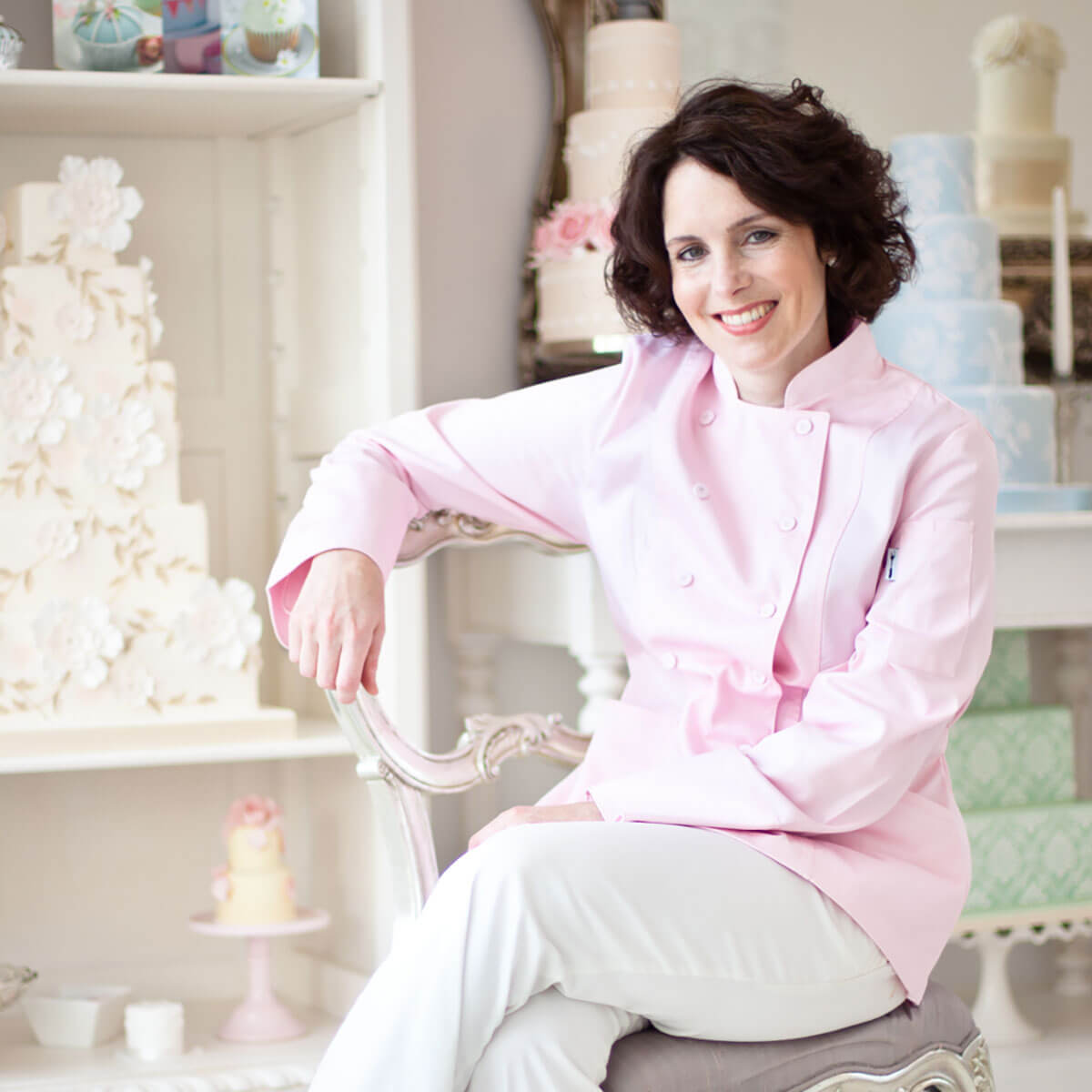 On-location lifestyle personal branding photography of a wedding cake designer seated in her studio, surrounded by display cakes