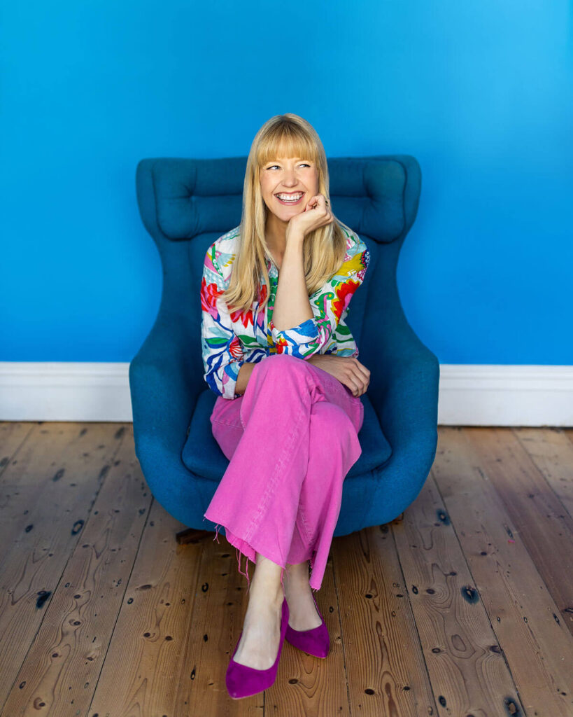 Professional headshots example from UK personal brand photographer, showing a female entrepreneur in colourful clothing on blue living room background