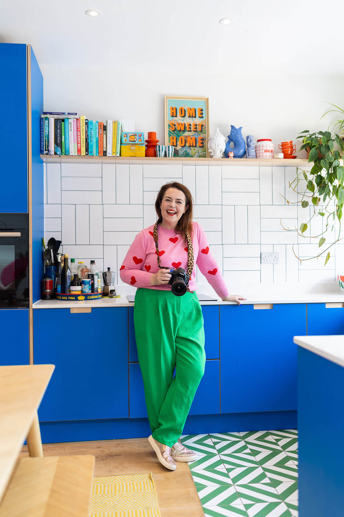 Rosie Parsons standing in a bright kitchen, holding a camera and smiling, representing guidance and support for business owners considering their next step in personal branding photography